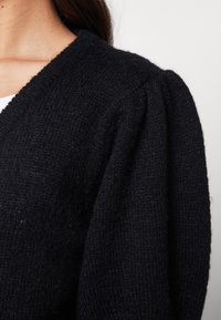 Černý pletený cardigan s texturovaným povrchem, výstřihem do V a nabíranými rukávy pro větší rozměr.