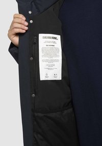 Vandafvisende jakke med sort inderfor og marineblå ydre lag. Har en lynlåslomme og plejeetiket på det indvendige foer. Textureret stof.