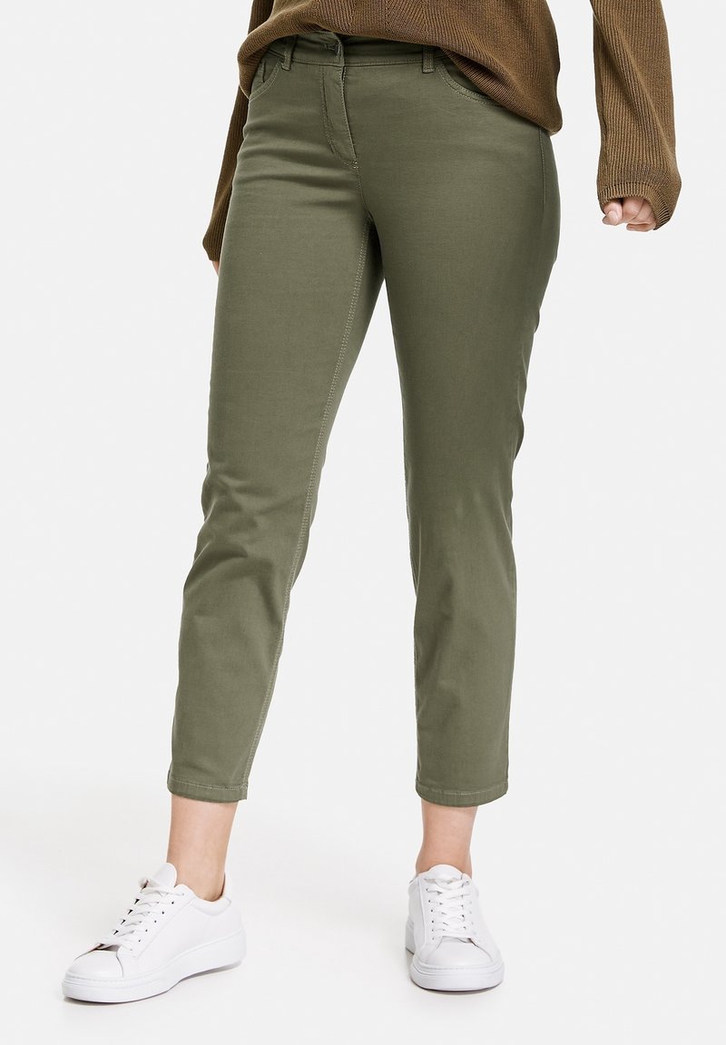 Olivgrön tapered byxor gjorda av bomullsblandat tyg med bältesöglor, framfickor och stiligt fåll, kombinerat med vita sneakers.