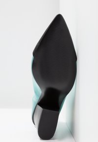 Une chaussure à talon aigu turquoise avec un bout pointu et une semelle en caoutchouc noir, présentant des détails texturés et un design courbé élégant.