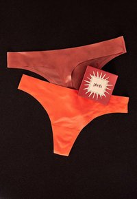 Deux strings sans coutures couleur rouille et orange vif avec une étiquette de marque Gisela rouge sur fond noir.