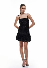 Miniabito nero con paillettes, spalline sottili, corsetto aderente, orlo arricciato svasato, texture lucida e silhouette sinuosa.