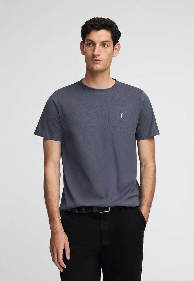 Grå bomullströja med rund hals och korta ärmar, med en liten vit logotyp på bröstet. Matchad med svarta byxor.