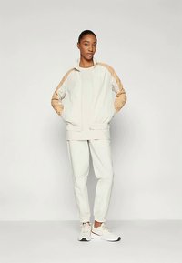 Hele beež jakk tumepruunide aktsentidega, varustatud tõmbluku ja elastsete varrukatega. Koos sobiva kitseneva püksiga ja valgete tossudega.