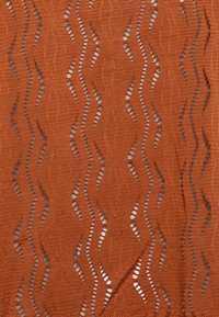 Brun spets tyg med ett vågmönster och öppna utskärningar, som visar en strukturerad yta och intrikata detaljer.