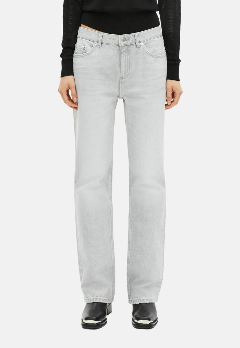 Persona con jeans rectos de color gris claro, top ajustado de manga larga negro y botines negros de punta cuadrada.