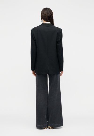 Μαύρο σακάκι με εφαρμοστή γραμμή και μία σχισμή στο πίσω μέρος. Συνδυασμένο με παντελόνι από σκούρο γκρι τζιν με φαρδιά πόδια και παπούτσια με animal print.