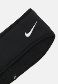 Juodas flisinis galvos apdangalas su siuvinėtu baltu Nike logotipu. Turi lygų išorę ir elastingą apdailą, kad puikiai priglustų.