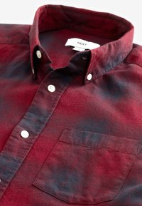 Camisa de cuadros roja y negra, tipo button-up, con cuello, bolsillo frontal y botones blancos, hecha de una tela suave con un acabado texturizado.