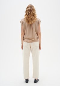 Beige, kortärmad blus med en lös passform, tillsammans med krämfärgade raka byxor. Svarta platta skor fulländar outfiten.