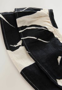Čiernobiely vzorovaný textil s abstraktnými tvarmi, vyrobený z bavlny. Má viditeľné stehy pozdĺž okrajov. Mäkčený, textúrovaný povrch.
