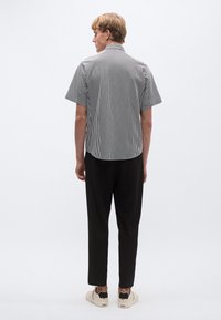 Cămașă cu mâneci scurte cu dungi alb-negru, cu croială lejeră, umeri lăsați și tiv curbat, combinată cu pantaloni negri și încălțăminte deschisă la culoare.