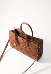 Bolso de mano de cuero marrón con diseño trenzado, doble mango superior, correa de hombro ajustable y acentos de hardware en tono dorado. Cuenta con cierre de cremallera.