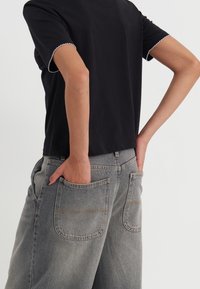 Maglietta nera con bordo bianco scallop alle maniche, abbinata a pantaloni larghi grigi chiari con grandi tasche posteriori.