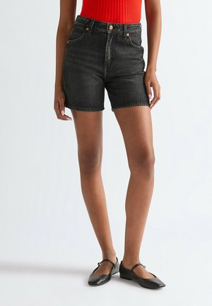 Sorte denimshorts med høj talje, fem lommer og et lige snit. Kombineret med en rød ribbet top og sorte ballerinaer.