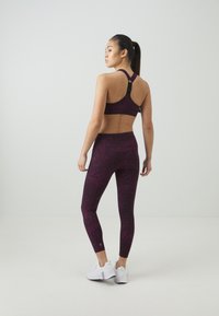 Vijolična športna modrc in ujemajoče se legice z teksturiranim leopardskim potiskom. Obleka ima dizajn z dirkaškim hrbtom in je v paru z belimi športnimi čevlji.