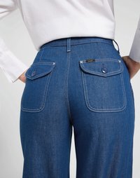 Calças de ganga azuis com cintura alta, dois bolsos traseiros com botões circulares e costura branca contrastante. Design de perna justa.