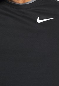 Camiseta deportiva negra de tela suave y texturizada, con cuello redondo y un pequeño logo blanco de Nike en la parte izquierda del pecho.
