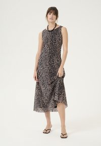 Rochie fără mâneci cu imprimeu leopard în nuanță bej și pete negre, având un tiv asimetric fluid și un material ușor. Pur tată cu sandale negre în stil flip-flop.