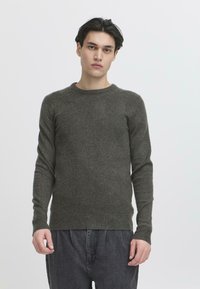 Pulover tricotat de culoare verde închis, cu mâneci lungi, gât rotund și manșete și tiv din tricot elastic. Textură moale cu o siluetă ajustată.