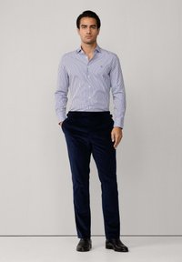 Hellblau-weiß gestreiftes Hemd mit Knopfleiste, kombiniert mit marinblauen Cordhosen und schwarzen eleganten Schuhen. Schlichtes Design, taillierte Silhouette.