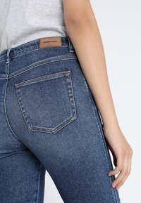 Blå denimjeans med en figurnära passform, featuring en läderlogotyp på baksidan och en standard bakficka med sömdetaljer.