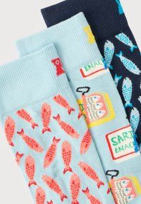 Τρία ζευγάρια πολύχρωμες κάλτσες με σχέδια ψαριών· ένα γαλάζιο με κόκκινα ψάρια, ένα γαλάζιο με κονσέρβες σαρδέλας, και ένα σκούρο μπλε με μπλε ψάρια.