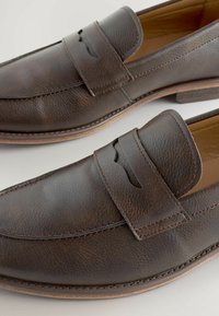 Pruunid nahast loafers, millel on tekstureeritud pind, silmapaistva õmbluse detail ja lõikeaktsent vampi piirkonnas. Lame talla disain.