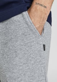 Sive pamukaste trenirke s glatkom teksturom, koje imaju bočne džepove i malu crnu oznaku sa natpisom "Jack & Jones."