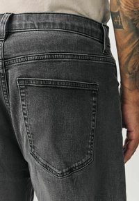 Svarte cowboybukser i denim med fem-lomme design, en lige pasform og synlige syninger. Stoffet virker let tekstureret og brugt.