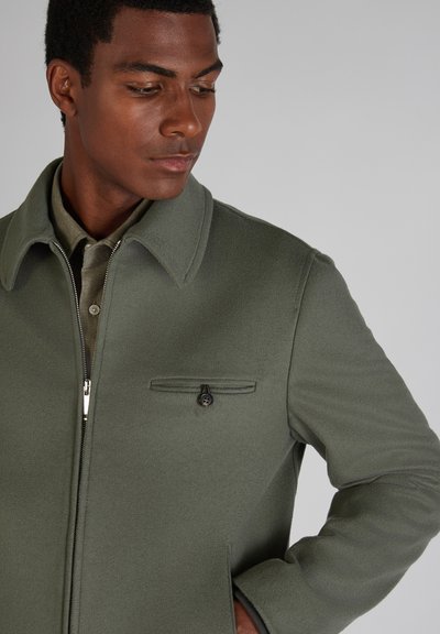 Olivgrünes Wollmischungsjackett mit umklappbarem Kragen, Frontreißverschluss und einer Brusttasche mit Knopf. Glatte Textur, taillierte Passform, minimalistisches Design.