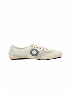 Zapatilla de corte bajo de color beige claro con paneles de malla, cordones beige y un logo circular oscuro en el lateral, sobre un fondo blanco.