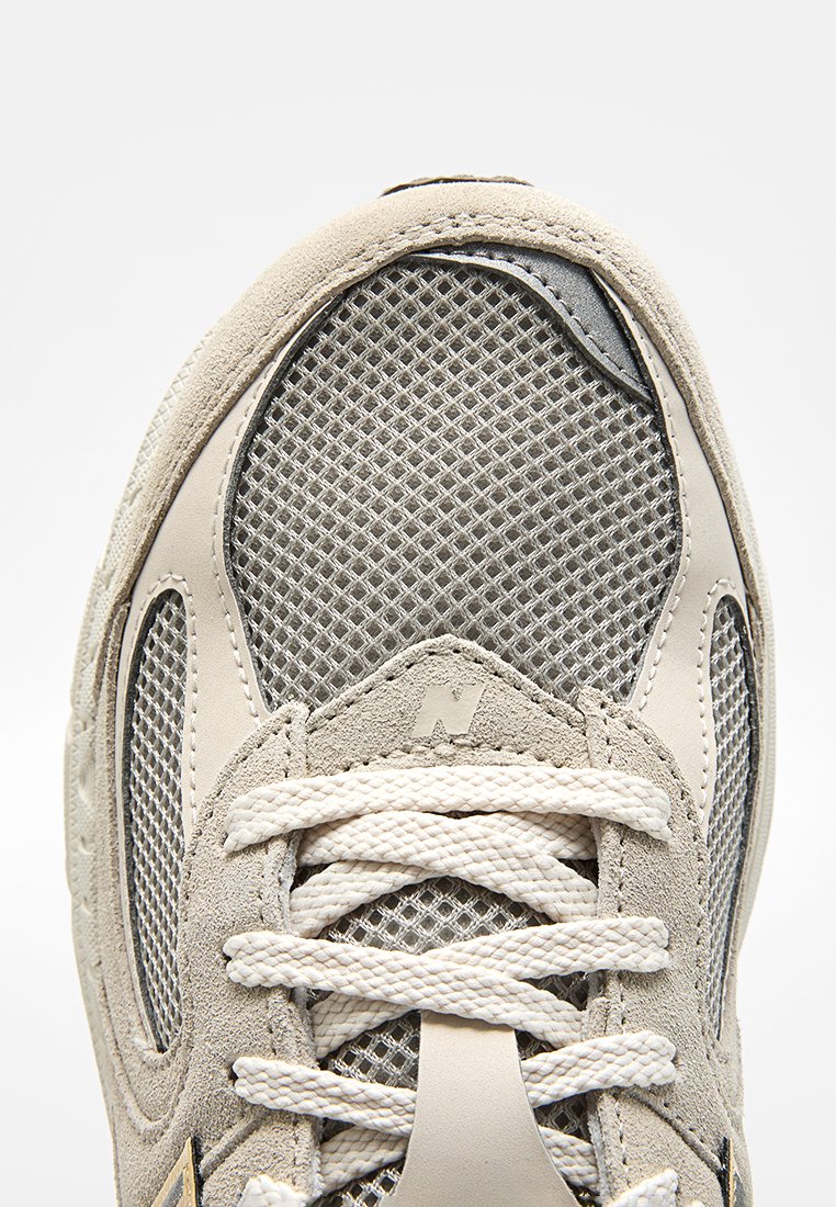 Primo piano della punta della sneaker in mesh beige e grigio con lacci bianchi e dettagli in suede, che evidenziano la texture e le cuciture.