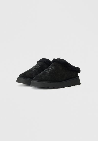 Sapatos slip-on de camurça preta com forro felpudo e sola texturizada. Bico arredondado e detalhe de costura subtil na parte superior.