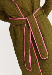 Prešívaný župan v olivovo zelenej farbe, zdobený vzorom listov, ružovým lemovaním a pásikom na zaväzovanie v rovnakom štýle. Materiál má textúrovaný, polstrovaný vzhľad.