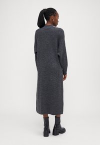 Μακρυφόρεμα σε σκούρο γκρι χρώμα, πλεγμένο με ραβδωτή υφή, με χαμηλούς ώμους, πλαϊνές σχισμές και στρογγυλή λαιμόκοψη, συνδυασμένο με μαύρες μπότες μέχρι τον αστράγαλο.