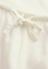Tissu en coton blanc avec une taille élastique et un cordon de serrage noué. La texture est lisse avec un léger éclat, montrant peu de rides.