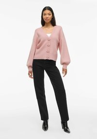 Roze, knoopsluiting cardigan met ballonmouwen, gebreide textuur, verfraaid met bloemvormige knopen, gecombineerd met zwarte rechttoe-rechtaan jeans.