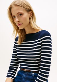 Μπλε ναυτικό και λευκό ριγέ μακρυμάνικο τοπ με λαιμόκοψη καραβόπανο, με μικρό λογότυπο, συνδυασμένο με ψηλόμεσο τζιν και καφέ ζώνη.