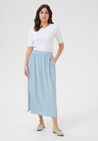 Lys blå maxiskørt med tekstureret overflade, elastisk talje, sidelommer og en slids. Sæt det sammen med en tætsiddende hvid T-shirt med korte ærmer.