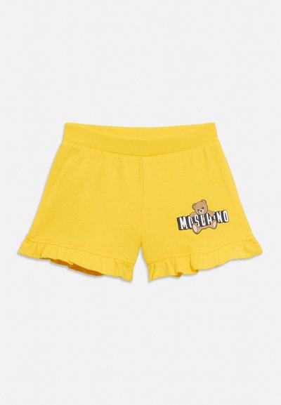 Short jaune pour enfants avec des ourlets à volants et un ours en peluche tenant un logo "Moschino" sur la jambe droite.
