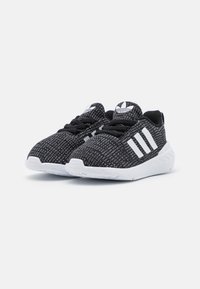 Scarpe da ginnastica nere con tomaia texturizzata, logo a tre strisce bianche, lacci neri e suola bianca con un motivo scanalato.