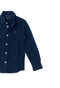 Camicia blu navy con bottoni, realizzata in tessuto intrecciato, dotata di colletto, maniche lunghe e un piccolo logo sul petto. Cinque bottoni bianchi.