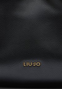 Sac en cuir noir avec une surface texturée. Logo doré "LIU-JO" affiché de manière proéminente en bas. Design simple et épuré.