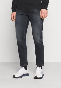 Jeans de ganga azul escuro com um corte slim e um leve desbotado, combinados com ténis brancos e cinzentos com uma sola texturada e detalhes em contraste.