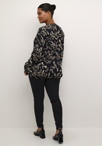 Blusa blu marina con motivo floreale beige, scollatura rotonda, maniche lunghe. Abbinata a jeans skinny neri e scarpe con tacco a blocco nere.