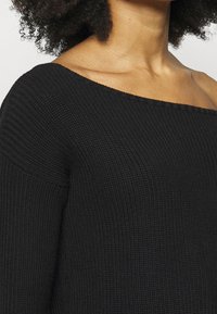 Černý pletený svetr s výstřihem přes ramena a strukturovanou tkaninou. Má žebrovaný vzor a volný střih.