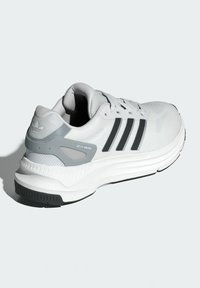 Zapatos Adidas ZX RS en blanco y gris, con una parte superior de malla texturizada, suela gruesa, tres rayas negras y un logo en la parte trasera.
