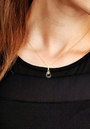 Collier en chaîne dorée avec un pendentif en perle noire en forme de goutte, présentant une texture lisse et un éclat subtil, reposant sur un haut noir.