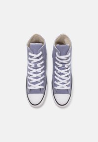 Světle fialové vysoké plátěné tenisky s bílými tkaničkami a gumovou špičkou. Mají černou gumovou podrážku a béžové vnitřní podšívku.